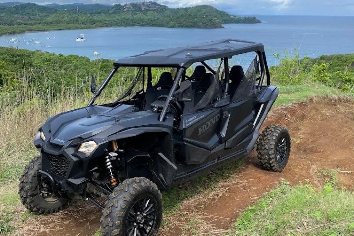Black off-road vehicle parked on grassy hill overlooking ocean and bay.