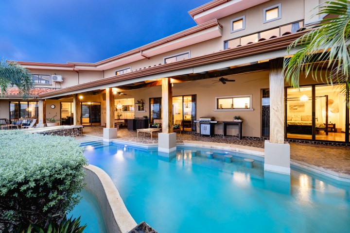 Modern house with swimming pool, patio, and outdoor seating at dusk.