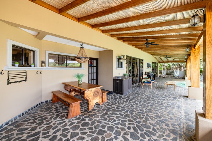 Outdoor patio with wooden ceiling, stone floor, dining set, and pool in view.