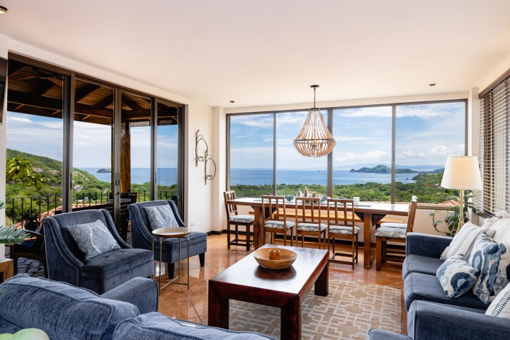Living room with ocean view, blue couches, wooden table, large windows, and decorative lighting.
