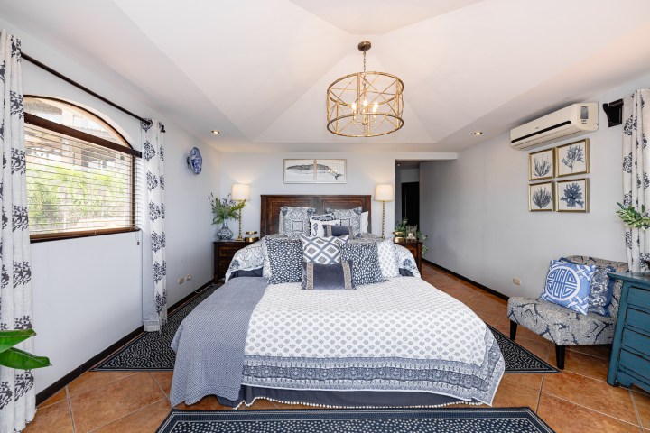 Modern bedroom with blue-white decor, patterned curtains, wall art, and large bed with pillows.