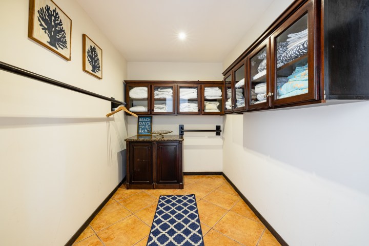 Walk-in closet with wooden cabinets, folded towels, clothes hanger, and framed artworks on beige walls.
