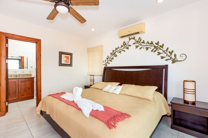 Cozy bedroom with double bed, wall decor, ceiling fan, and view into a bathroom.