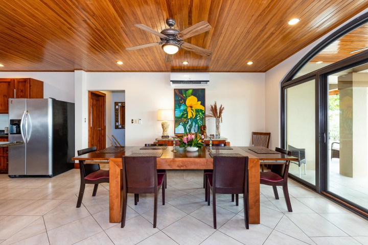 Dining room with wooden ceiling, table, chairs, colorful painting, ceiling fan, and glass doors.