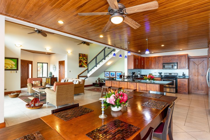 Open-plan kitchen and living room with wood ceiling, ceiling fans, wooden furniture, and decorative flowers.
