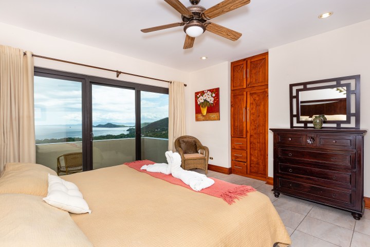Bedroom with ocean view, bed, dresser, wardrobe, and ceiling fan.