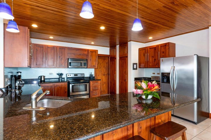 Modern kitchen with wooden cabinets, granite countertops, stainless steel appliances, and blue pendant lights.