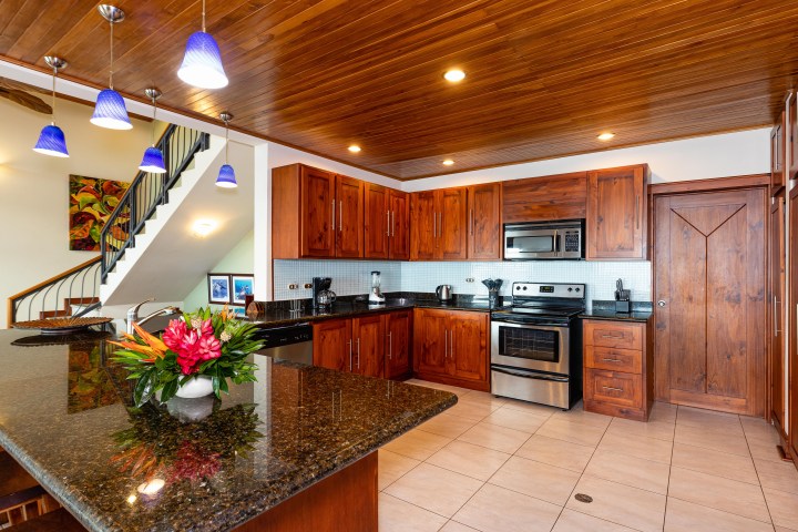 Modern kitchen with wooden cabinets, stainless steel appliances, and a granite island with flowers.