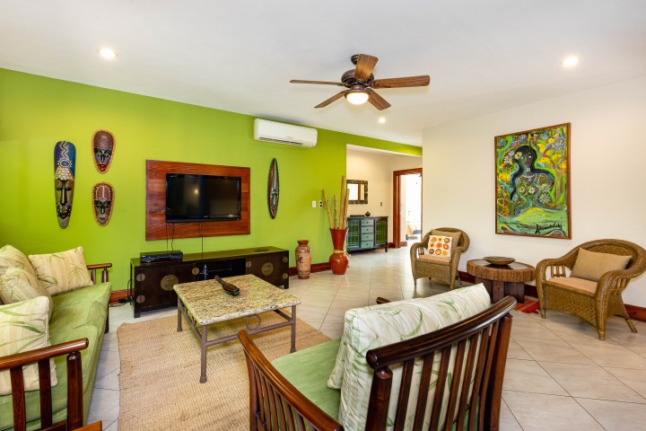 Living room with green accent wall, TV, art, wicker furniture, and ceiling fan.