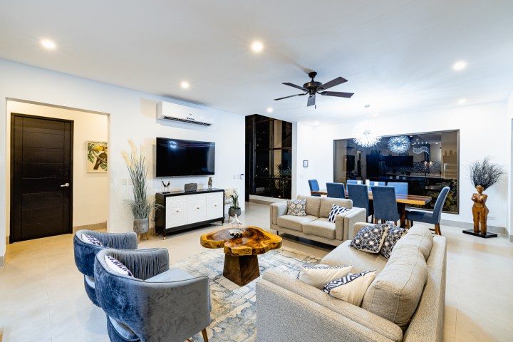 Modern living room with gray sofas, wooden table, blue chairs, and TV on the wall.