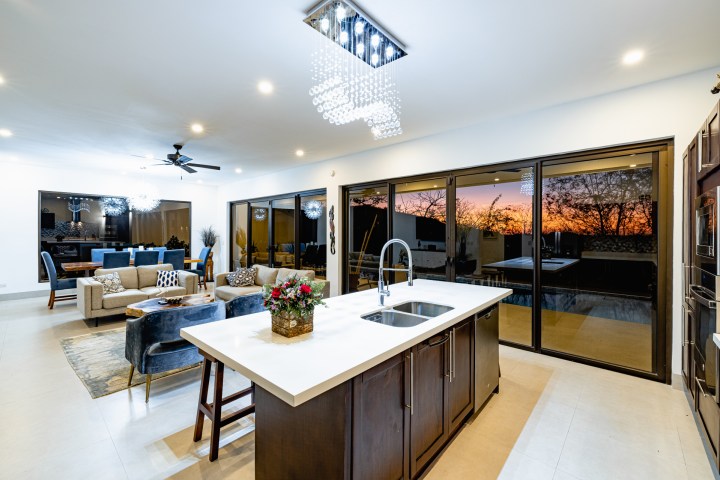 Modern kitchen with island, living room, large windows, and sunset view.