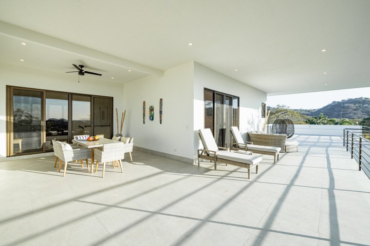 Spacious terrace with wicker furniture, lounge chairs, and mountain view.