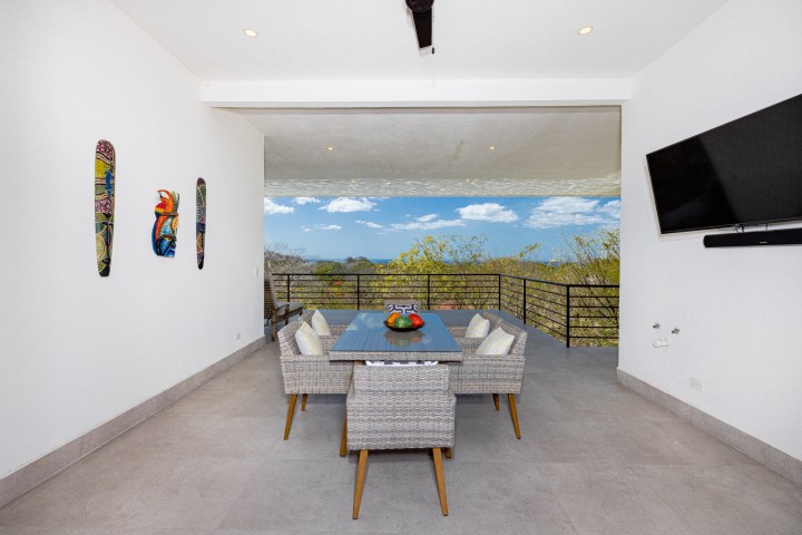 Outdoor seating area with a table, chairs, wall art, and a view of trees and sky.