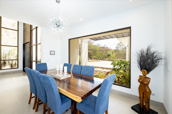Dining room with blue chairs, wooden table, large window, modern lamp, and decorative sculpture.