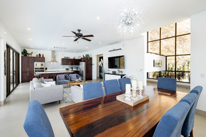 Modern open living space with dining table, blue chairs, kitchen, and large window with natural light.