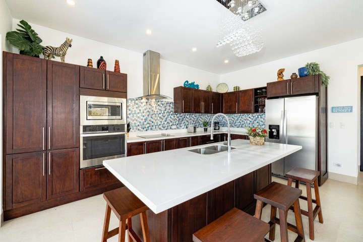 Modern kitchen with dark cabinets, island, stainless steel appliances, and blue patterned backsplash.