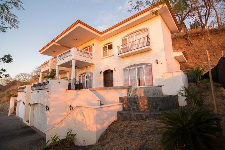 Two-story house with balconies, white walls, and stone steps at sunset.