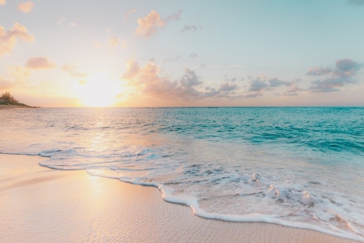 a man walking across a beach next to the ocean