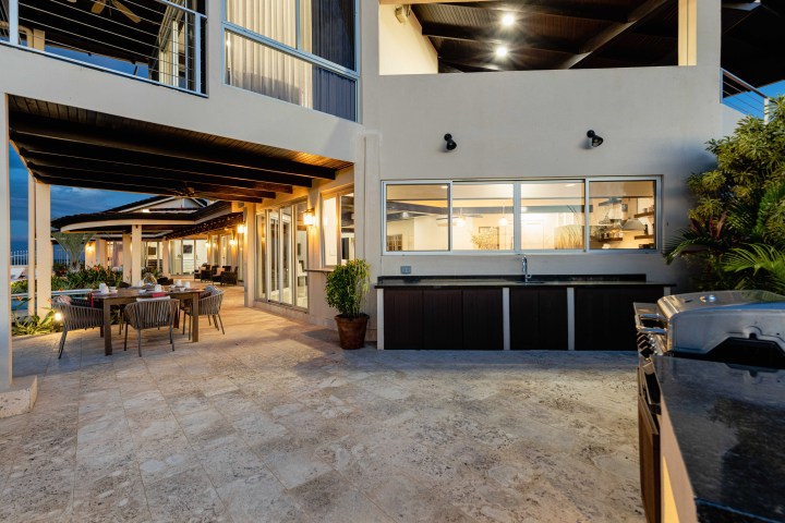Outdoor patio with dining table, chairs, and built-in barbecue next to a modern house at dusk.