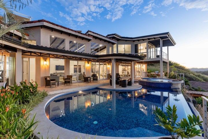 Luxury house with a large swimming pool and outdoor seating, set against a scenic sunset.