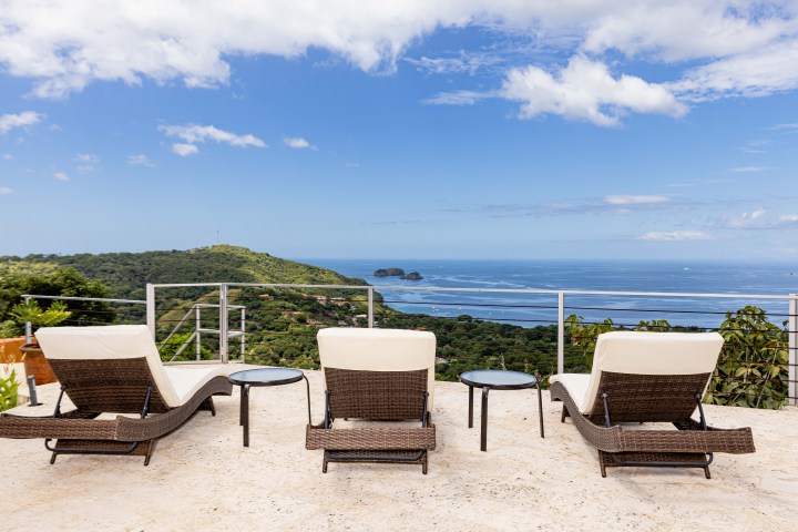 Three lounge chairs on a terrace overlooking a lush landscape and ocean view.
