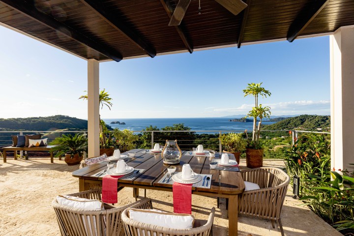 Outdoor dining area with ocean view, set table, and surrounding greenery under a canopy.