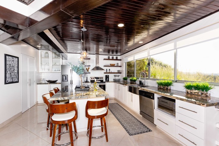 Modern kitchen with brown ceiling, island, stools, and plants on counters.