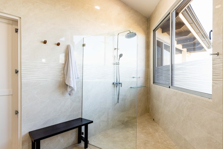 Modern bathroom with glass shower, towel, bench, and large window.