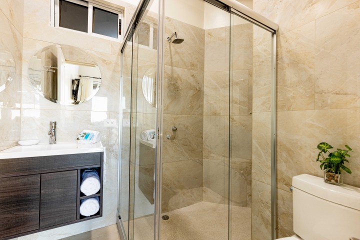 Modern bathroom with glass shower, round mirror, vanity, and potted plant on toilet.