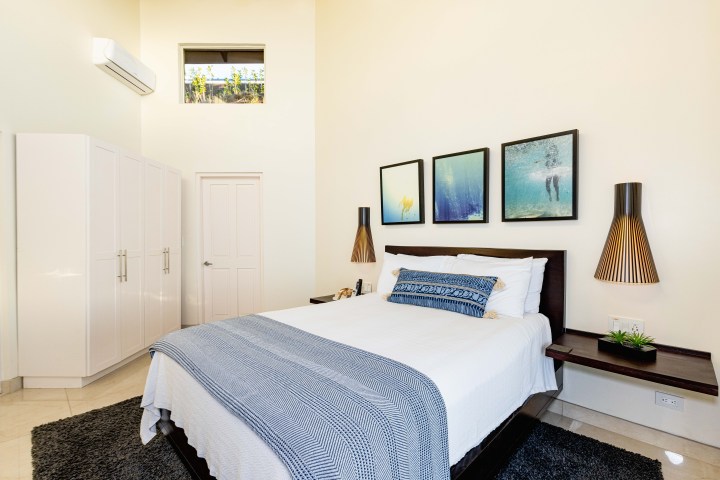 Modern bedroom with white bedding, blue throw, wall art, and minimalist decor.