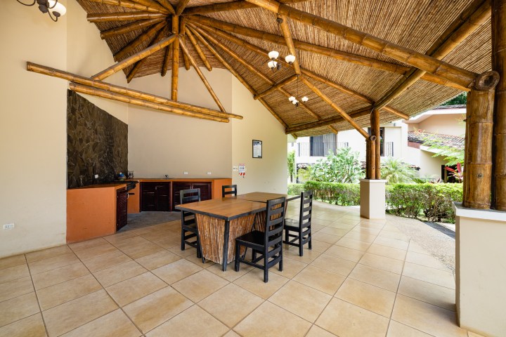 Open-air room with bamboo roof, dining table, chairs, and foliage view.