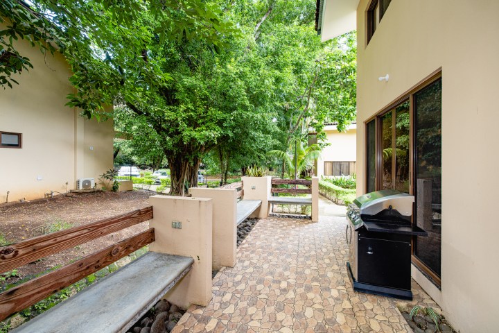 Outdoor patio with grill, benches, and trees beside a building.