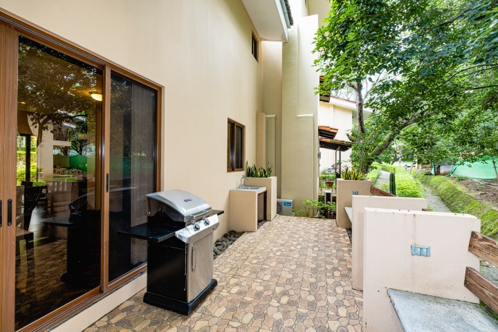 Outdoor patio with barbecue grill, sliding glass door, and view of trees.