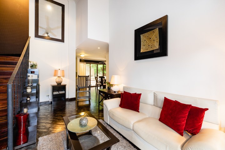 Contemporary living room with white sofa, red pillows, glass coffee table, and artwork on wall.