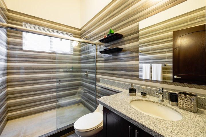 Modern bathroom with striped tiles, glass shower, and granite countertop.