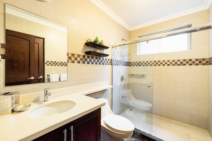 Modern bathroom with glass shower, sink, and wall mirror; shelves and checkered tile accent.