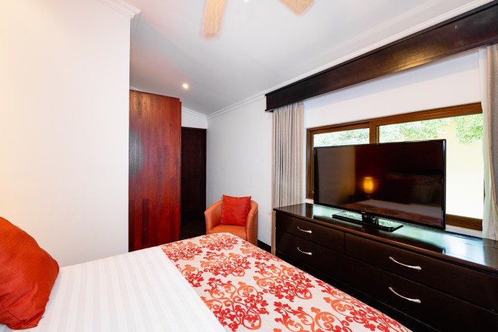 Bedroom with red accents, TV on dresser, window with curtains, and orange chair.