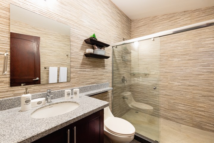 Modern bathroom with granite countertop, large mirror, glass shower, and wooden shelves.