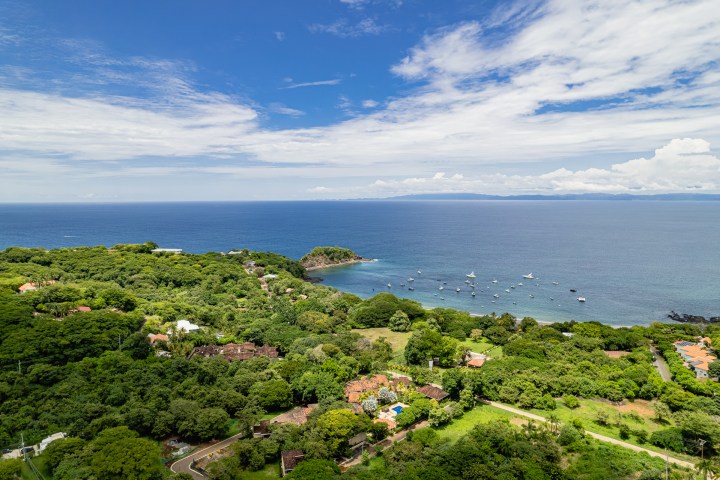 Aerial view of a lush green coastal area with boats near the shore under a blue sky.