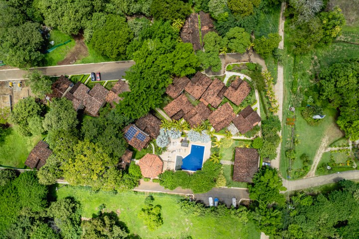 Aerial view of houses with red roofs, trees, a swimming pool, and landscaped gardens.