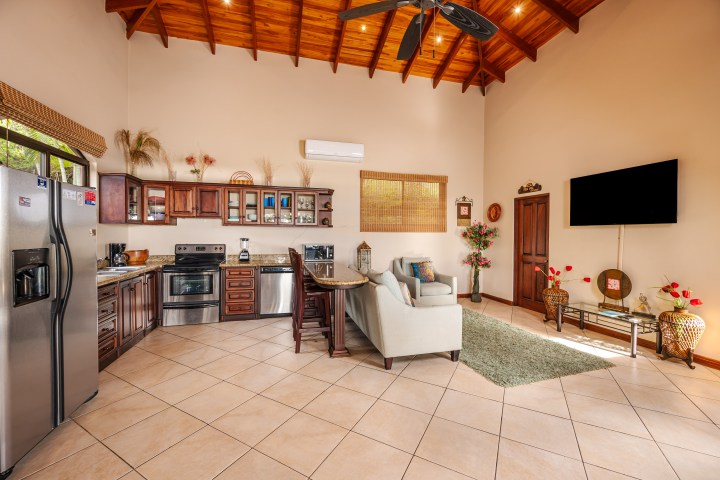 Open living room and kitchen with wooden ceiling, sofa, TV, and stainless steel appliances.