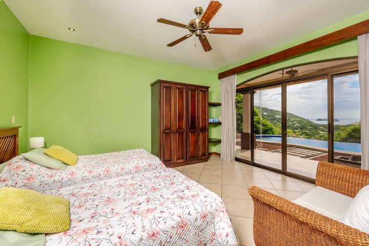 Bedroom with green walls, twin beds, wooden wardrobe, wicker chair, sliding doors, and ocean view.