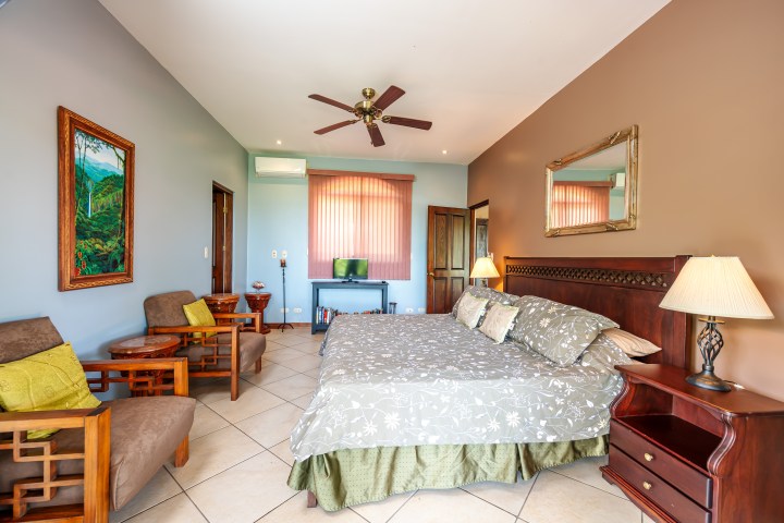 Spacious bedroom with a double bed, armchairs, and a ceiling fan.