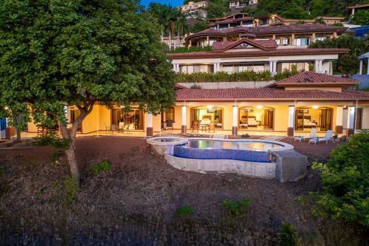 Luxury hillside villa with pool, surrounded by lush greenery at dusk.
