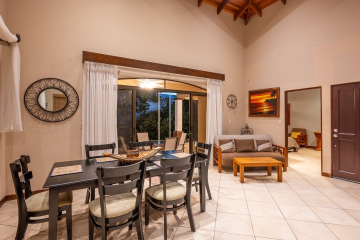 Dining area with table, chairs, a sofa, and a wall mirror, adjacent to sliding doors and a doorway.