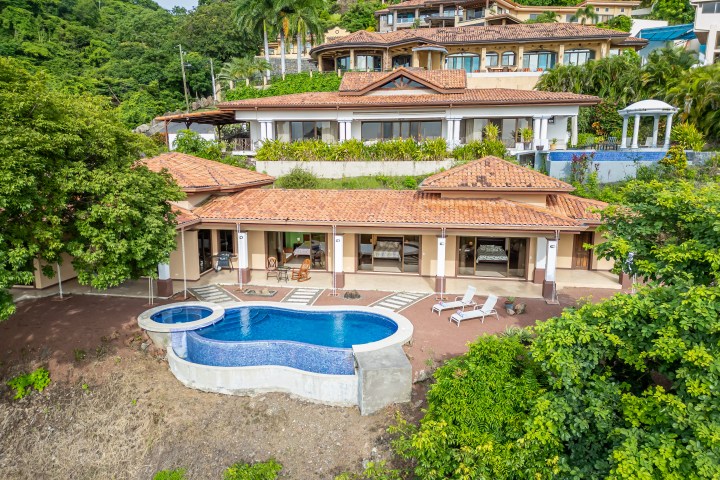 Hillside villa with terracotta roof, pool, surrounded by lush greenery.