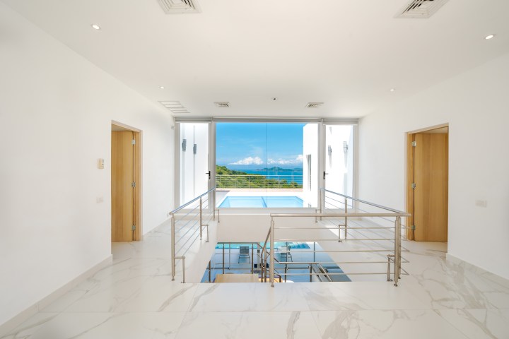 Bright hallway leading to balcony with ocean view, white marble flooring, and wooden doors.