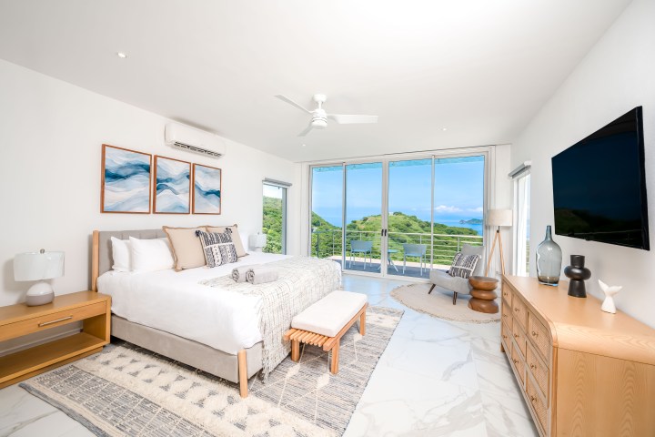 Modern bedroom with large bed, ocean view, and balcony access through glass doors.