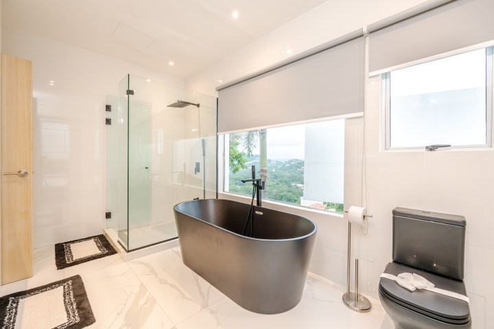 Modern bathroom with black bathtub, glass shower, and a scenic window view.