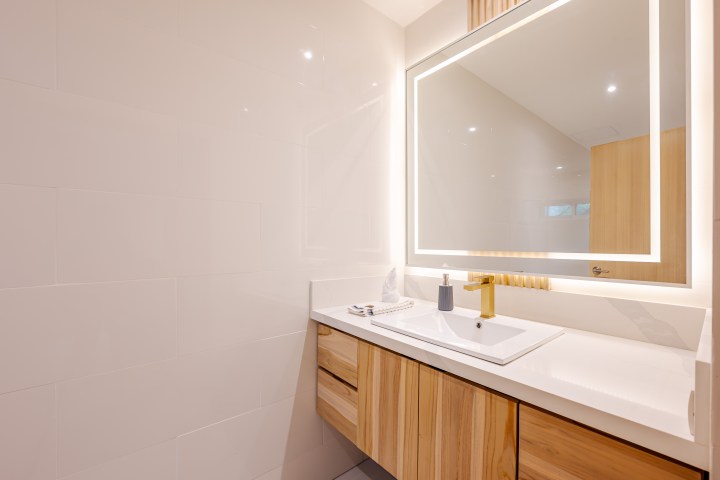 Modern bathroom with illuminated mirror, white sink, and wooden cabinets.